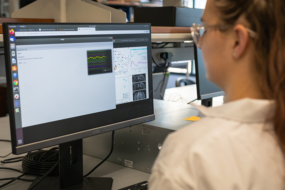 Texas BME student wearing lab safety gear and looking at computer in lab