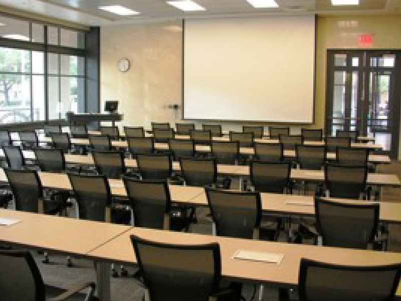 An empty conference room with large projector screen and rows of tables in BME 3.204