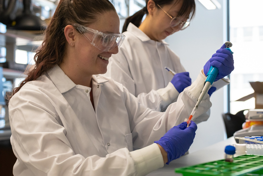 Two women in lab coats with droppers and beakers