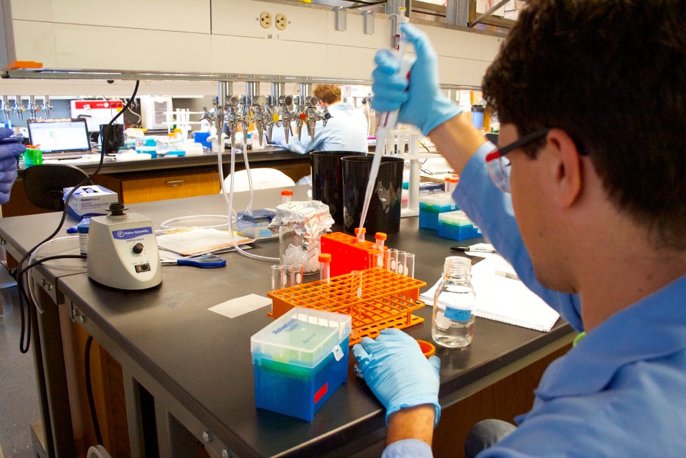 Student using liquid dropper to conduct research with samples in a lab space.