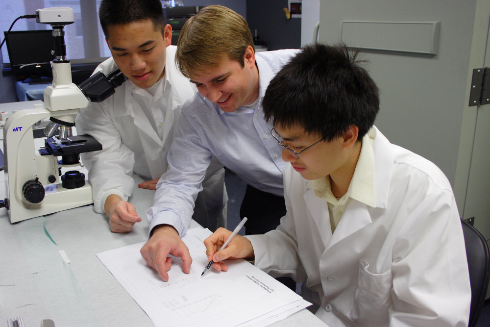UT Austin Biomedical Engineering students in a lab work on a document next to a microcope