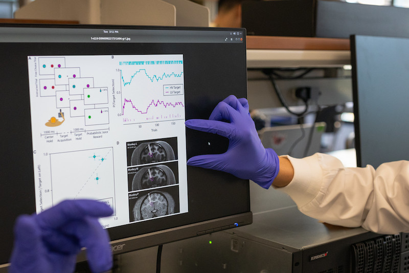 student's gloved hand pointing at computer screen with unintelligible data on it