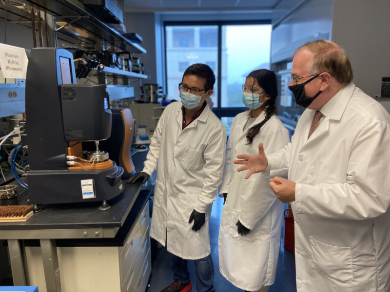 Professor Nicholas Peppas in lab coat standing in lab with students