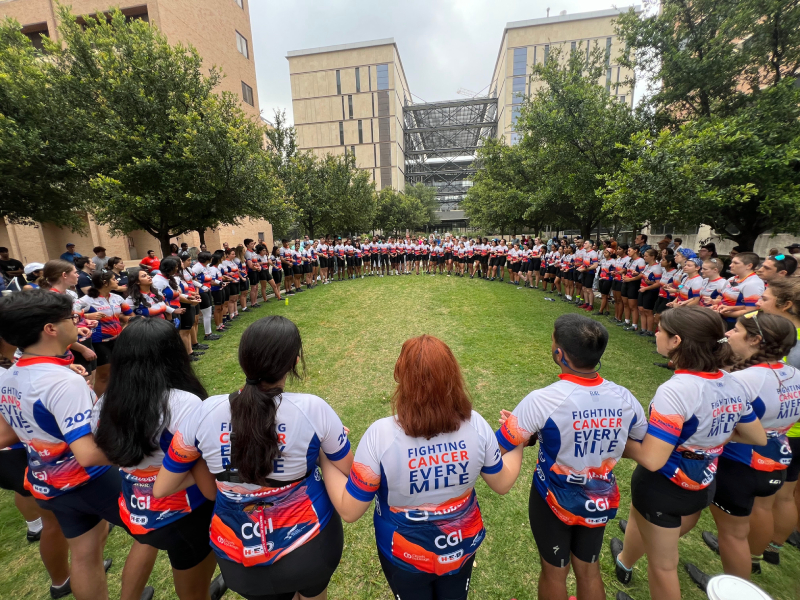 Cyclists for Texas 4000 stand in circle on a lawn holding hands