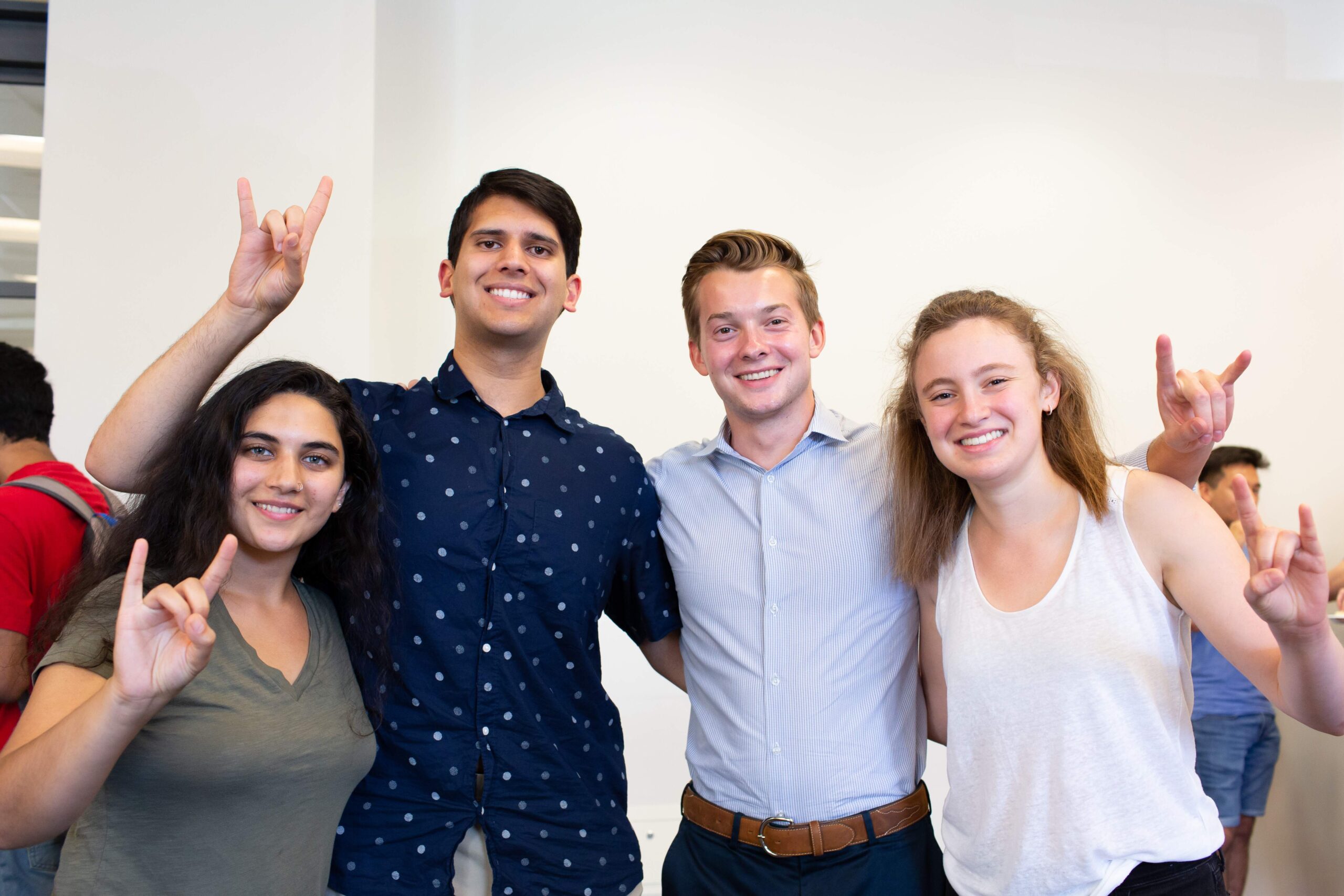 Four smiling students with a hook em hand sign