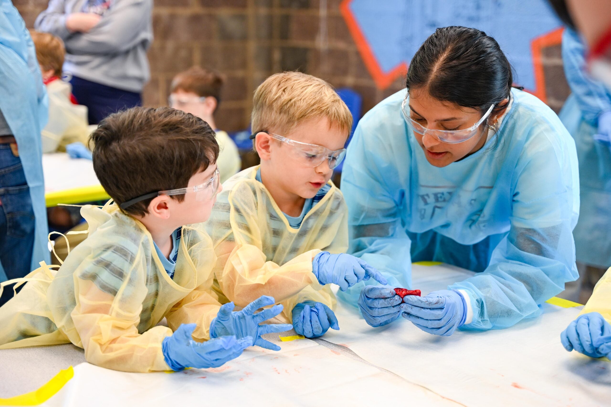 Two children in PPE gowns look at a sample of lung tissue held by a UT BME student in PPE during a Learning Lab hosted by the Science Mill
